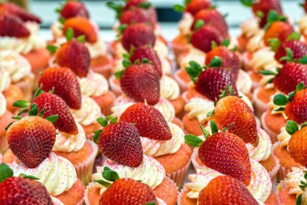 A close-up view of strawberry topped cupcakes with pink frosting, epitomizing sweetness and indulgence.